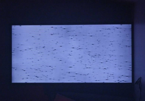 Electroluminescent emission from a CIGS panel shows a pinstripe pattern with dark local imperfections indicating possible local short circuits.