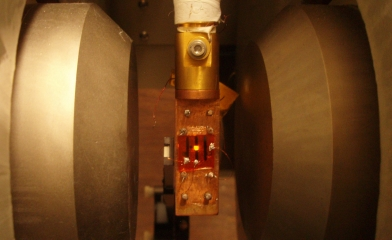 A spintronic OLED glows orangish (center) when the device, chilled well below freezing, is exposed to a magnetic field from the two poles of an electromagnet located on either side of the device.