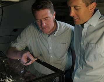 NIST physicists Scott Diddams (left) and Scott Papp show a prototype atomic clock based on a chip-scale frequency comb. Diddams is holding the silicon chip, which fits into the clock apparatus on the table. With performance improvements and further reductions in size, the technology could eventually be used to make portable tools for measuring time and frequency.