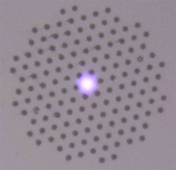 This optical fiber has been infused with hydrogen and cured with UV light (here shown transmitting violet laser light). Fibers treated this way can transmit stable, high-power UV laser light for long periods of time, resisting the damage usually caused by UV light. The diameter of the pattern of air holes surrounding the core is 62.5 &micro;m.