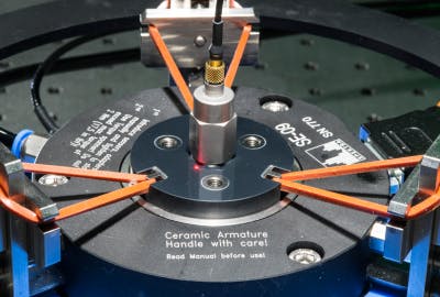 An accelerometer under test (hexagonal object) is attached to a shaker-table disk at the center of the apparatus. The red dot on the table surface is from the laser-interferometric vibrometer above (not shown).