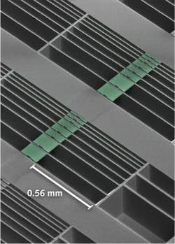 A scanning electron microscope image shows an array of optomechanical accelerometer devices with differing test-mass sizes. Highlighted green areas represent proof masses suspended by nanoscale tethers across the open, etched areas of the chip. The nanobeam cavities are seen as small square notches in the centers of the masses.