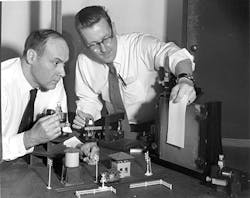 FIGURE 1. Emmett Leith (left) and Juris Upatnieks prepare to record a hologram in 1965. The model railroad set became a standard scene.