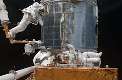 Shuttle Atlantis mission STS-125 upgrades Hubble a final time in May 2009. Mission specialist Andrew Feustel at left rides on the end of the remote manipulator arm as mission specialist John Grunsfeld at bottom signals to him.