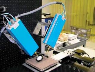 A laboratory raster-scanning millimeter-wave setup for imaging land mines includes VNA radiation sources and detectors (blue boxes), a soil-filled specimen stage, and polyethylene lenses (just above the stage).