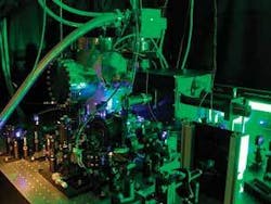 FIGURE 1. A scanning photoionization microscope (SPIM) includes an optical microscope (in vacuum chamber, background) and an ultrafast laser (appears as blue, foreground). FIGURE 1. A scanning photoionization microscope (SPIM) includes an optical microscope (in vacuum chamber, background) and an ultrafast laser (appears as blue, foreground).