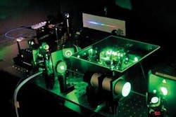 FIGURE 2. A modelocked Ti:sapphire laser (center) generates a frequency comb. The green light is scattered from the diode-pumped doubled-neodymium pump laser at right. The frequency comb is projected onto a screen in background; it looks like a rainbow-spanning continuum at this resolution. FIGURE 2. A modelocked Ti:sapphire laser (center) generates a frequency comb. The green light is scattered from the diode-pumped doubled-neodymium pump laser at right. The frequency comb is projected onto a screen in background; it looks like a rainbow-spanning continuum at this resolution.