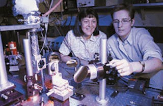 Researchers Deborah Sivco (top left) and Claire Gmachl (top right) monitor a lab experiment containing a bidirectional semiconductor laser. A two-wavelength version of the laser emits light at 6.33 &micro;m with a positive bias and 6.5 &micro;m with a negative bias; wavelength varies with temperature (bottom). Longitudinal mode structure spans a width of 0.3-0.5 nm.