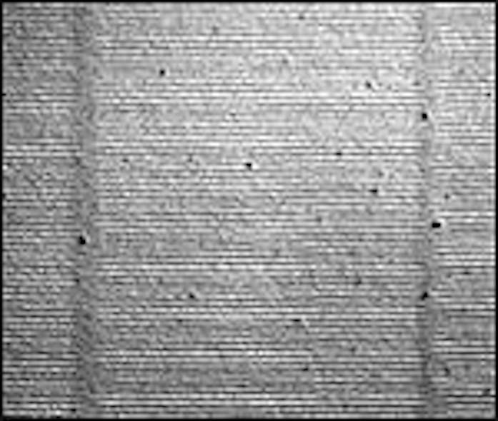 Atom lithography creates structures using a standing-wave light field resulting from three beams as the mask. An optical micrograph shows 426-nm-period gold structures (bright regions) after processing. Two vertical hazy lines spaced by 23.4 mm arise from an interruption of the horizontal lines. The researchers attribute the vertical lines to multiple interference of the three light beams.