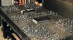To verify the effectiveness of a distributed tuned mass damping system, 350 individual dampers distributed in frequency were applied to the corners and center region of an optical table. The masses of the dampers totaled 37 kg; no tuning was involved. In the commercial version, fewer dampers wil be used, and the dampers will be mounted inside the table structure. The rectangular objects are 55-lb masses used to load the table.
