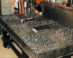 To verify the effectiveness of a distributed tuned mass damping system, 350 individual dampers distributed in frequency were applied to the corners and center region of an optical table. The masses of the dampers totaled 37 kg; no tuning was involved. In the commercial version, fewer dampers wil be used, and the dampers will be mounted inside the table structure. The rectangular objects are 55-lb masses used to load the table. To verify the effectiveness of a distributed tuned mass damping system, 350 individual dampers distributed in frequency were applied to the corners and center region of an optical table. The masses of the dampers totaled 37 kg; no tuning was involved. In the commercial version, fewer dampers wil be used, and the dampers will be mounted inside the table structure. The rectangular objects are 55-lb masses used to load the table.