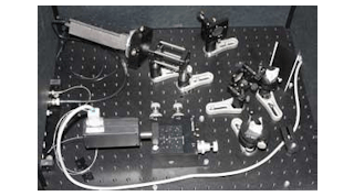 A lithium niobate waveguide (bottom left) combines a pump laser and a near-IR signal, up-converting the signal to a visible wavelength. Two prisms (right) separate the signal from the combined beam and send the signal to an avalanche-photodiode detector (top left), which reads the upconverted signal.