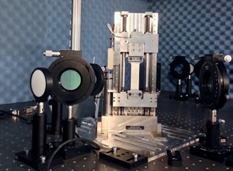 A tensile machine pulls a metal specimen with a ceramic thermal barrier coating sprayed on its surface. With a polariscope, changes in refractive index resulting from this applied strain can be measured. Some of the components of the gigahertz polariscope are seen on either side of the tensile machine.