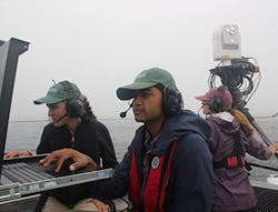 Johns Hopkins University Applied Physics Laboratory (APL) free-space optical (FSO) operators check the monitors on Sea Hunter as a third operator monitors operations. The FSO system can be seen at top right. Johns Hopkins University Applied Physics Laboratory (APL) free-space optical (FSO) operators check the monitors on Sea Hunter as a third operator monitors operations. The FSO system can be seen at top right.