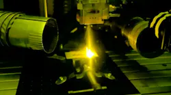 Inside NIST's laser welding booth, a high-power laser melts a piece of metal to form the letters NIST.