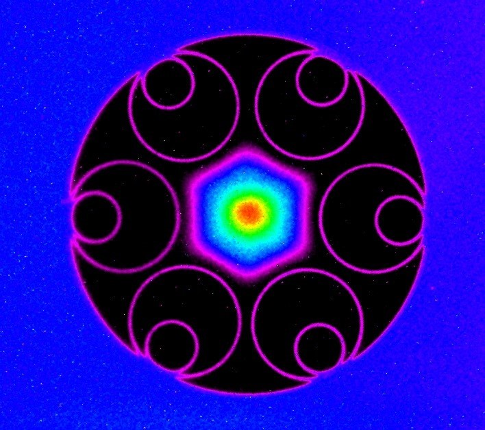 Microscopic cross-section of the record-setting low-loss hollow-core fiber. Thin hollow glass cylinders shown in pink run the length of the fiber, effectively creating bars that prevent the hexagonal light modes trapped in the center of the air-filled core from leaking into the glass. The hollow core, defined by the inner edges of the cylinders, is 37 &micro;m across.