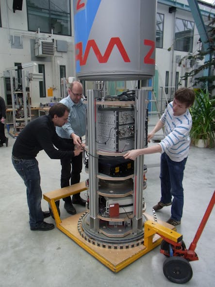 FIGURE 4. Capsule containing Menlo Systems&rsquo; frequency comb system is prepared for tests in an evacuated 120-m drop tower at the University of Bremen. The optical head is the black module at center; electronics for the comb system are above it. The three lower platforms carry other equipment used in the experiment.