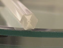 A PHOSFOS photonic-crystal fiber (shown here as a preform) will be patterned with Bragg gratings and be embedded in a flexible polymer skin for sensing (top). An experimental polymer skin, illuminated with a supercontinuum source, is wrapped around a surface to be monitored (bottom).