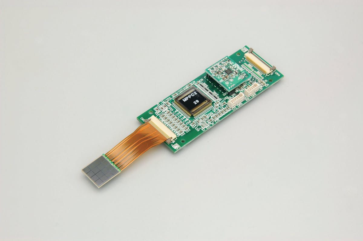 FIGURE 4. Shown here is an MPPC module that makes use of the monolithic 4 &times; 4-channel array on flex cable. The electronics include a high-voltage power supply, temperature compensation circuit, and two ASICs mentioned in the text.