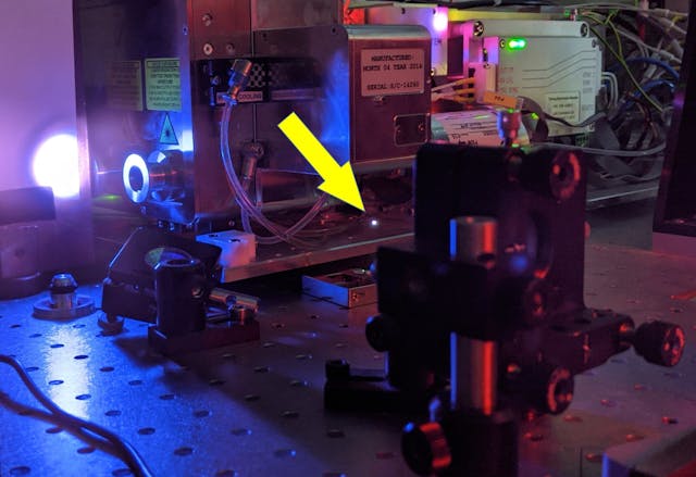 FIGURE 2. Breakdown of air (small bright spot indicated by the yellow arrow) induced by 400 &micro;J pulses from a 100 kHz Yb:KGW laser; the large white spot on the screen in the background is white-light continuum generated in air.