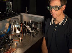 NIST engineer Tasshi Dennis sits next to NIST&apos;s solar simulator based on a white-light supercontinuum laser. The instrument simulates sunlight to help measure the properties of solar cell materials. The instrument&apos;s beam is illuminating a gallium arsenide solar cell in the lower left corner of the photo.