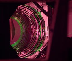 An Advanced LIGO optic has a mass of about 40 kg; about half of the cylindrical optic can be seen. The green light comes from an alignment laser. The maze-like patterns are actuators that translate, tip, and tilt the optic to maintain its alignment.