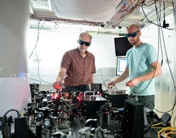 FIGURE 1. Optical system for the NIST trapped-ion sensor with physicists John Bollinger (left) and Matt Affolter (right). Cryogenics and a powerful superconducting magnet are inside the pillar at left. FIGURE 1. Optical system for the NIST trapped-ion sensor with physicists John Bollinger (left) and Matt Affolter (right). Cryogenics and a powerful superconducting magnet are inside the pillar at left.