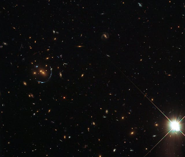 FIGURE 1. An image from the Hubble telescope shows a luminous red galaxy cluster to the left of center, surrounded by bluish arcs of more distant galaxies whose light has been bent by the gravitational pull of the cluster.