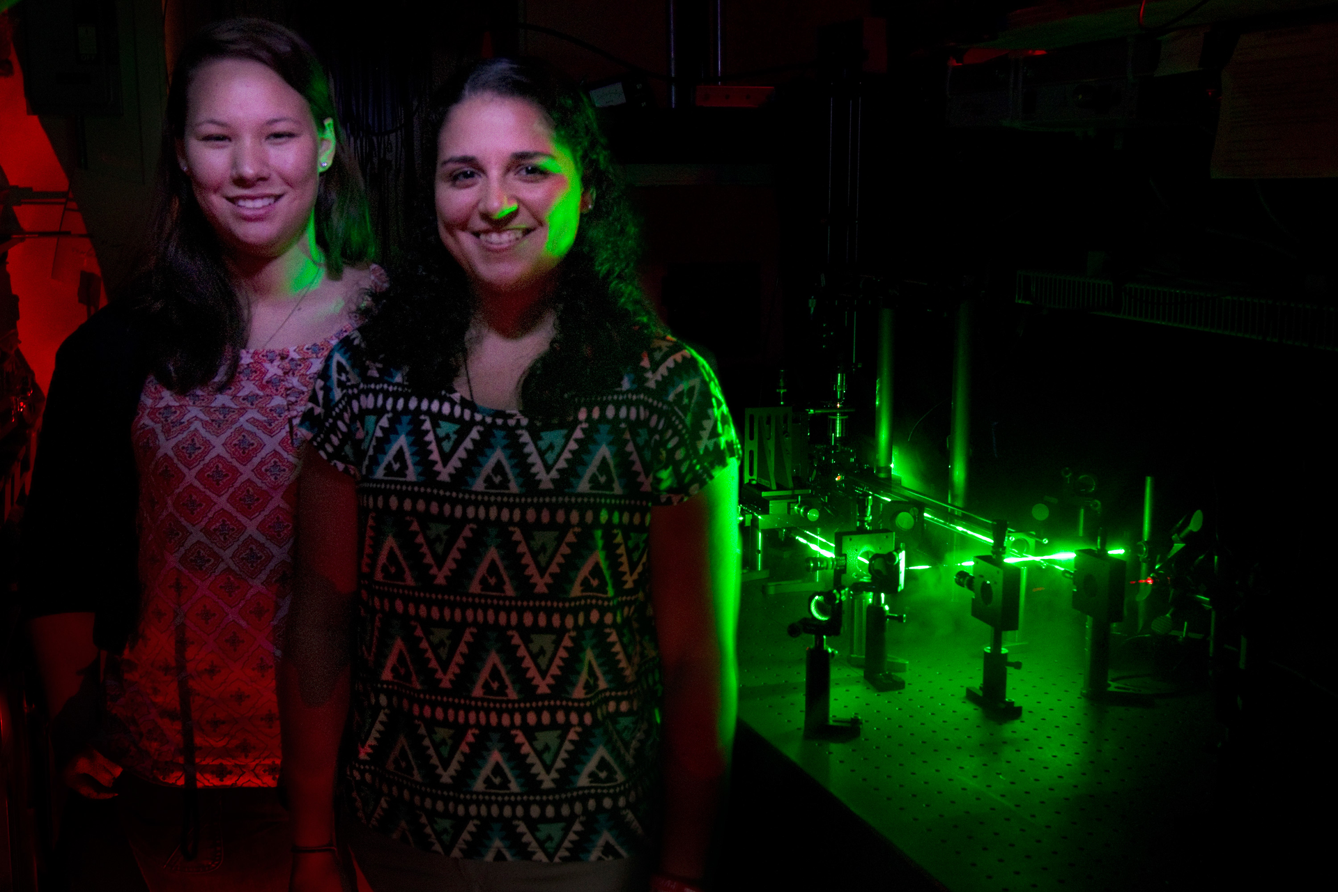 Angela 'Nikki' Chang and Jessica Barrios stand in front of an optical tweezers apparatus that Chang is using to study nanoparticles used in cancer therapy.