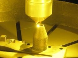 FIGURE 2. Metal powder is blown through nozzles to the focal point of a laser, forming a molten pool that is moved to form the part layer by layer. FIGURE 2. Metal powder is blown through nozzles to the focal point of a laser, forming a molten pool that is moved to form the part layer by layer.