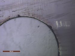 FIGURE 3. A 2 mm hole cut in carbon fiber composite shows virtually no thermal damage to the surrounding epoxy resin. FIGURE 3. A 2 mm hole cut in carbon fiber composite shows virtually no thermal damage to the surrounding epoxy resin.
