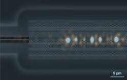 FIGURE 2. Scattered light imaged for a localized mode, composited to scale on top of a scanning electron microscope image of the waveguide. These modes are a signature of strong backscattering, which stops light input from the strip waveguide on the left from propagating further in the topological waveguide. FIGURE 2. Scattered light imaged for a localized mode, composited to scale on top of a scanning electron microscope image of the waveguide. These modes are a signature of strong backscattering, which stops light input from the strip waveguide on the left from propagating further in the topological waveguide.