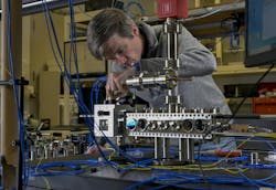 Jonathan Kwolek attaches fiber-optic cables to send light into a compact laser system, which is aligned around a custom vacuum cell. It generates a cold, continuous atomic beam, which is delivered to a larger vacuum chamber to address the Navy’s inertial navigation challenges. Jonathan Kwolek attaches fiber-optic cables to send light into a compact laser system, which is aligned around a custom vacuum cell. It generates a cold, continuous atomic beam, which is delivered to a larger vacuum chamber to address the Navy’s inertial navigation challenges.