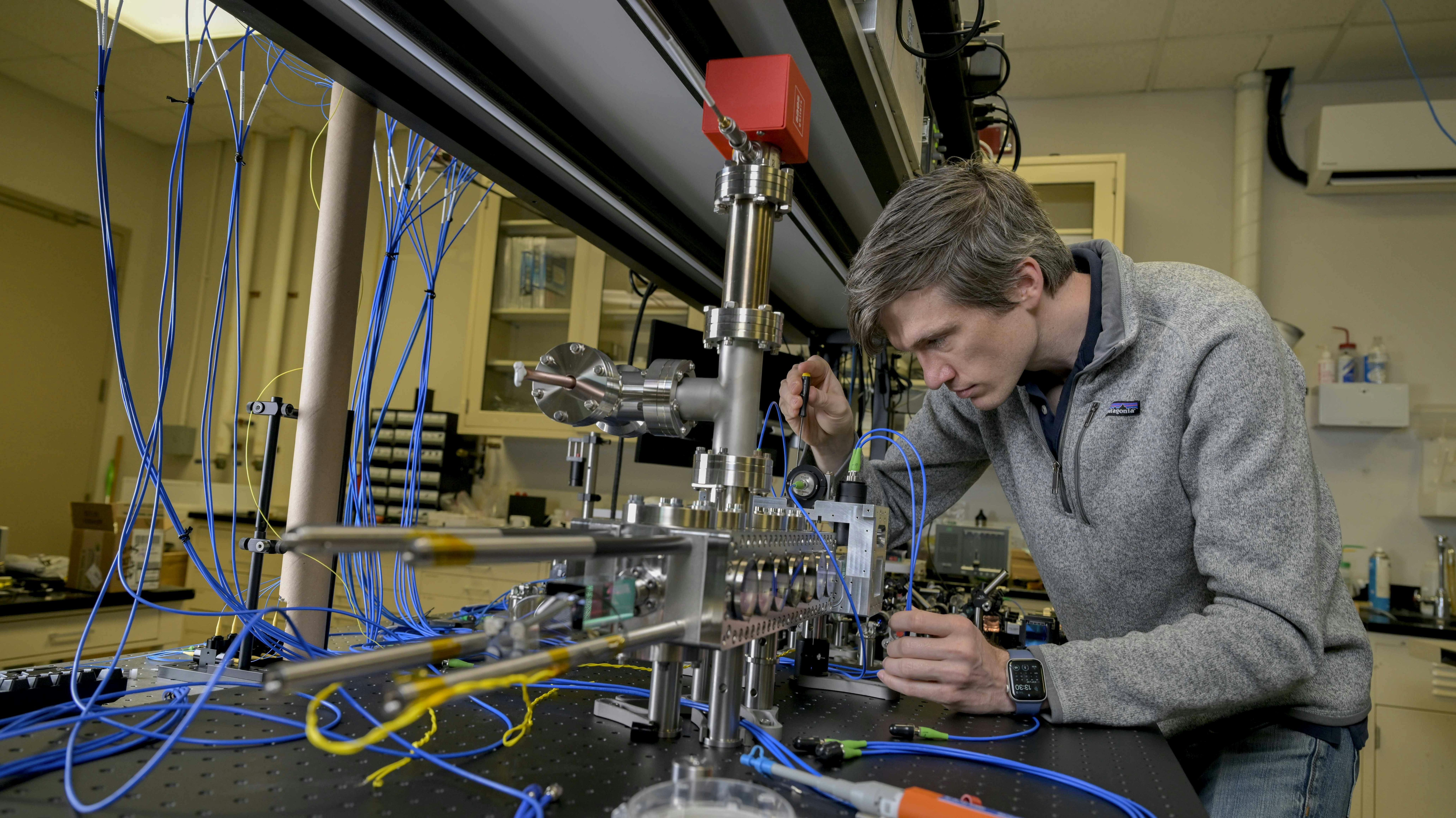 Jonathan Kwolek places a light-delivery system carefully around a custom vacuum chamber to align the optics within the custom light-delivery system to optimize the atomic beam in the NRL Atom Interferometry Lab.
