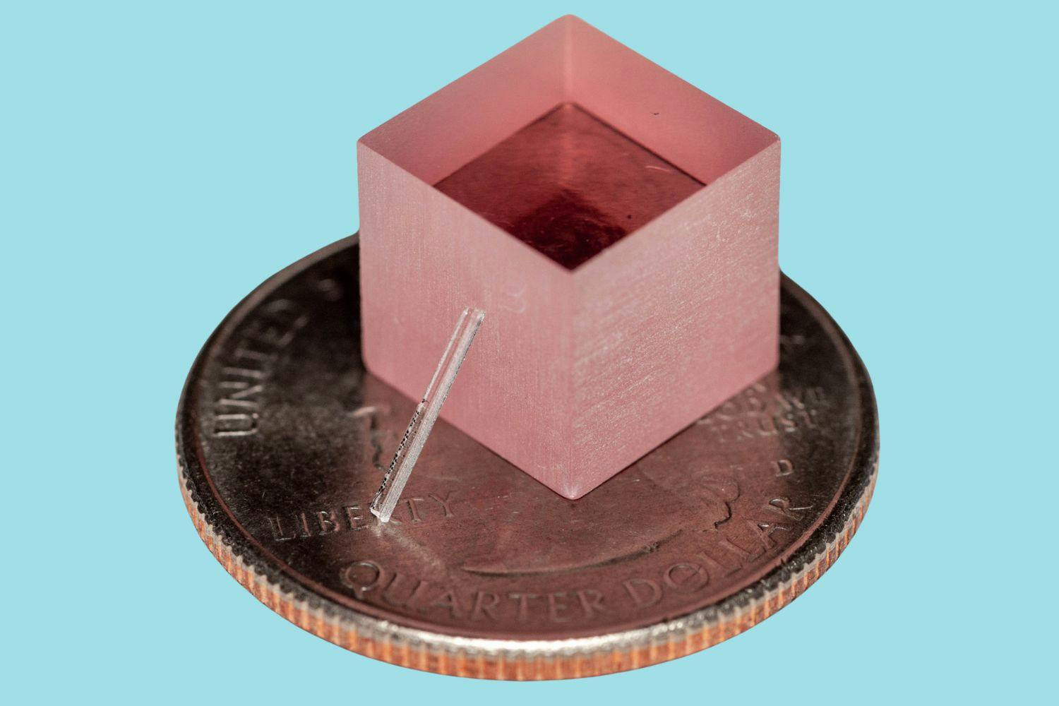 The group&rsquo;s new laser leans against a block of titanium-sapphire, and both are shown atop a quarter for scale.