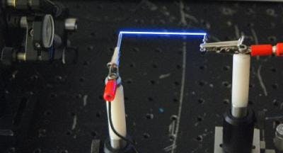 A femtosecond laser creates a thin column of plasma in the air between two electrodes.