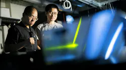 FIGURE 1. Li He (left) and Bo Zhen (right) in the lab with their photonic crystal platform that enables guiding light in a forward-only direction around a chip’s defects and bends. Credit: Eric Sucar/University of Pennsylvania