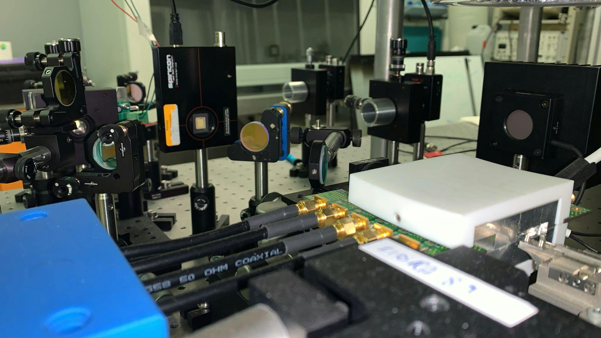 FIGURE 1. Measurement setup at Professor Lobino&rsquo;s quantum lab at the University of Trento; the chip is inside an oven to control its temperature, while electric signals reach the device through the black SMA cable. Credit: University of Trento